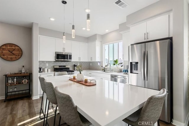 kitchen featuring a center island, white cabinetry, stainless steel appliances, sink, and hanging light fixtures