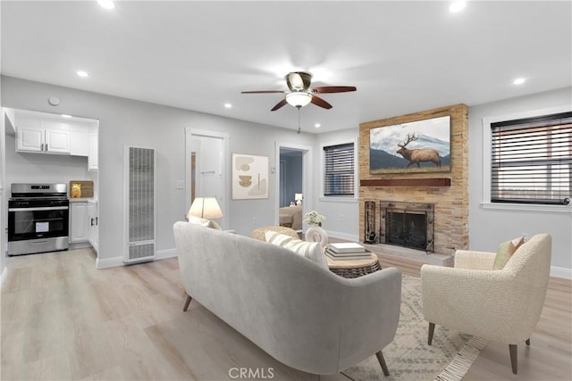 living room with ceiling fan, a fireplace, and light hardwood / wood-style floors