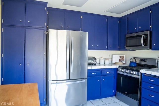 kitchen featuring light tile patterned floors, stainless steel appliances, and blue cabinets