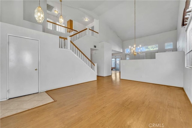 unfurnished living room featuring a chandelier, light wood-type flooring, and high vaulted ceiling