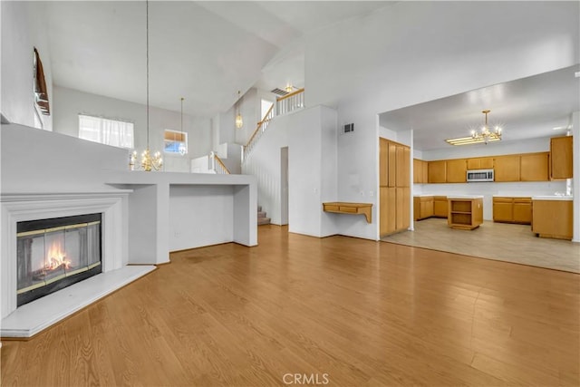 unfurnished living room featuring a towering ceiling, an inviting chandelier, and light hardwood / wood-style flooring