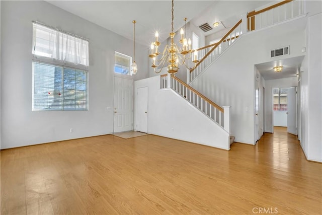 unfurnished living room featuring wood-type flooring, a towering ceiling, and a chandelier