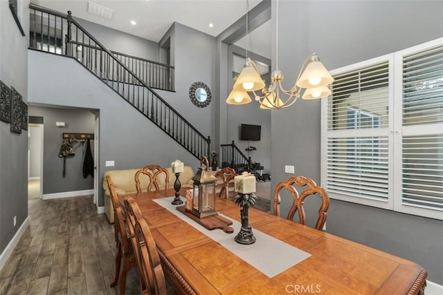 dining space with a towering ceiling, dark hardwood / wood-style floors, and a notable chandelier