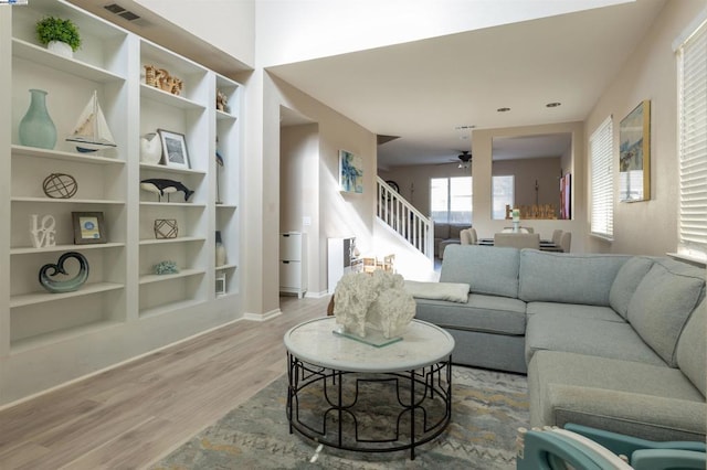 living room featuring ceiling fan, built in shelves, and light hardwood / wood-style flooring