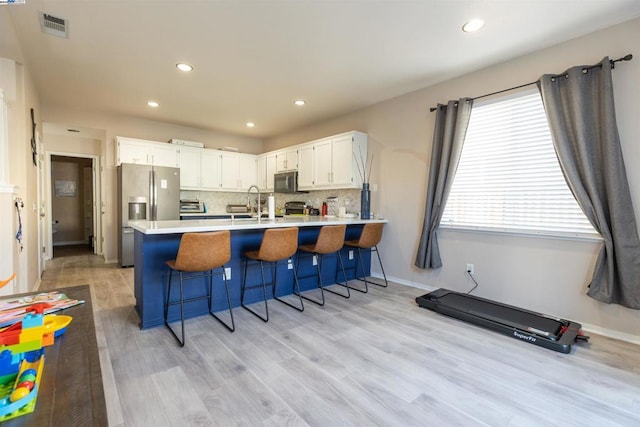 kitchen with white cabinets, a kitchen bar, stainless steel appliances, kitchen peninsula, and light hardwood / wood-style flooring