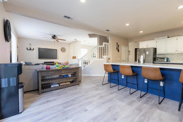 kitchen featuring white cabinets, a kitchen bar, light hardwood / wood-style floors, decorative backsplash, and stainless steel refrigerator