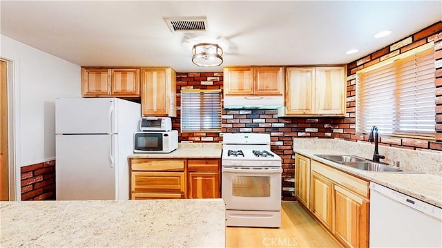 kitchen featuring white appliances, under cabinet range hood, a sink, light wood-style floors, and visible vents