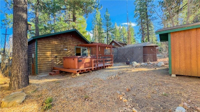 rear view of property featuring a wooden deck, an outdoor structure, and a hot tub