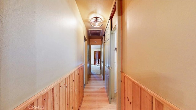 hall featuring a wainscoted wall, visible vents, light wood finished floors, and wooden walls