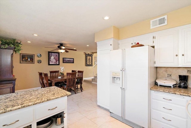 kitchen featuring white refrigerator with ice dispenser, white cabinets, ceiling fan, tasteful backsplash, and light stone counters