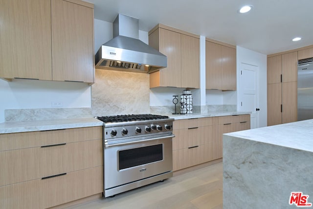 kitchen with premium appliances, light wood-type flooring, wall chimney range hood, and light brown cabinetry