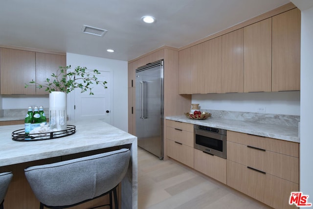 kitchen with a kitchen breakfast bar, light brown cabinets, light wood-type flooring, and stainless steel appliances