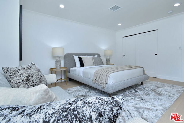 bedroom featuring hardwood / wood-style floors, crown molding, and a closet