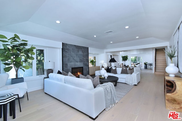 living room with a raised ceiling, a fireplace, and light hardwood / wood-style floors