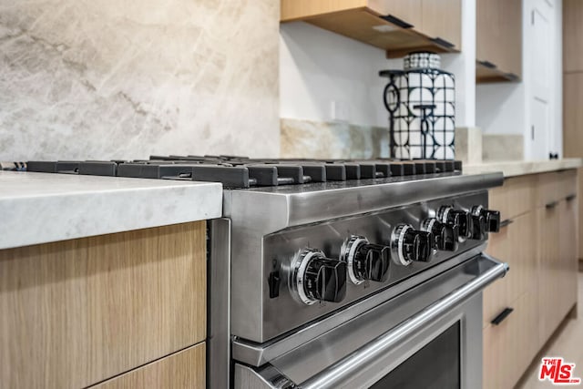 interior details featuring light brown cabinets, high end stove, and tasteful backsplash