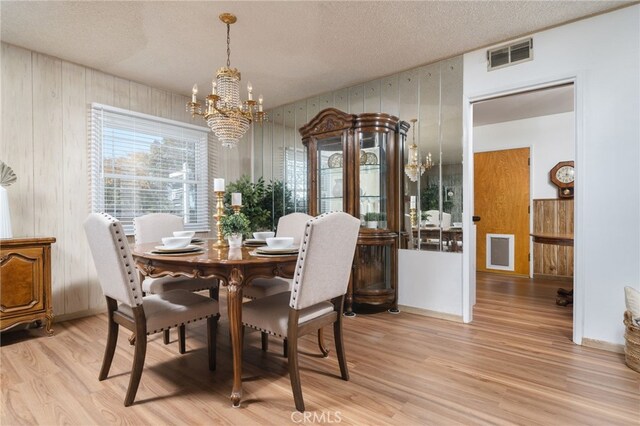 dining room featuring wooden walls, light hardwood / wood-style floors, a textured ceiling, and a notable chandelier