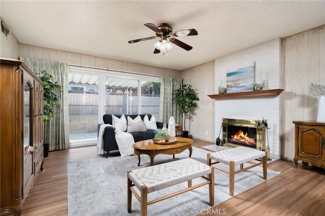 living room with ceiling fan, a fireplace, a textured ceiling, and light wood-type flooring