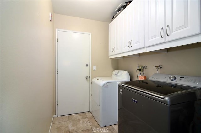 clothes washing area with cabinets, light tile patterned floors, and washer and dryer