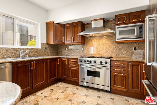 kitchen featuring wall chimney range hood, sink, decorative backsplash, light stone countertops, and premium appliances