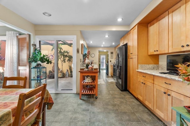 kitchen with stainless steel fridge, light stone countertops, and light brown cabinets