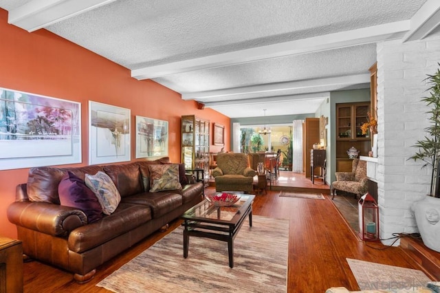 living room featuring an inviting chandelier, lofted ceiling with beams, wood-type flooring, a textured ceiling, and a fireplace