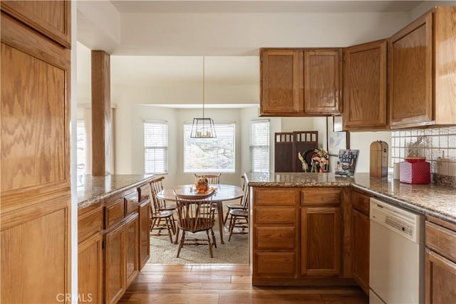 kitchen with tasteful backsplash, dark stone counters, white dishwasher, hardwood / wood-style floors, and hanging light fixtures