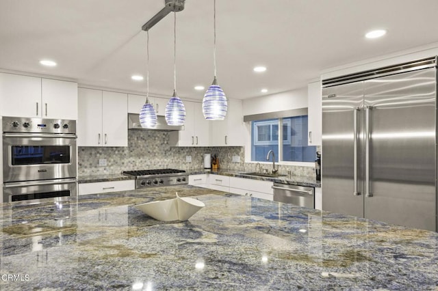 kitchen with appliances with stainless steel finishes, dark stone counters, sink, decorative light fixtures, and white cabinetry