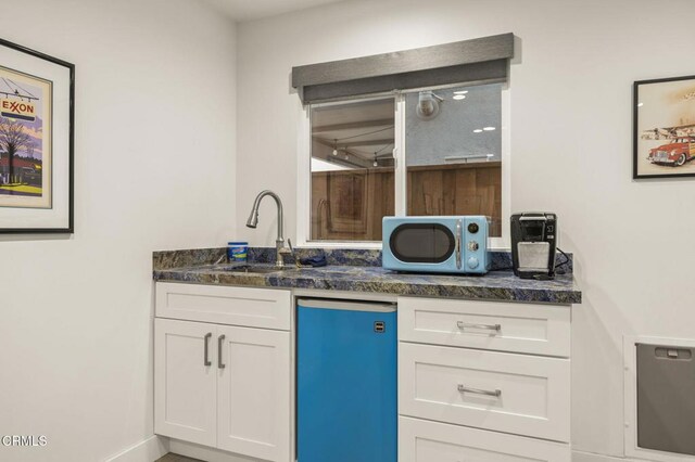 kitchen with stainless steel fridge, white cabinetry, sink, and dark stone counters