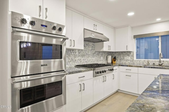 kitchen featuring white cabinetry, sink, dark stone countertops, light hardwood / wood-style floors, and appliances with stainless steel finishes