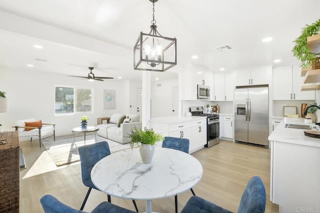 dining space with light hardwood / wood-style floors, ceiling fan with notable chandelier, and sink