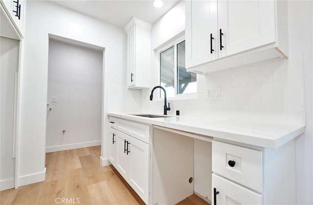 kitchen featuring light stone countertops, light hardwood / wood-style flooring, white cabinets, and sink