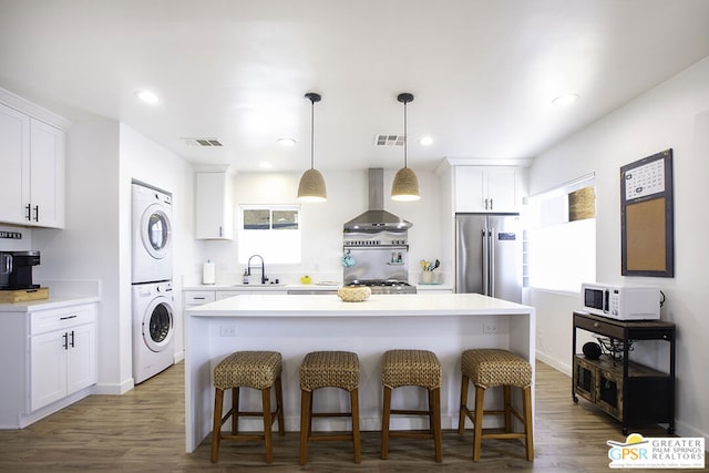 kitchen with white cabinetry, a center island, wall chimney exhaust hood, stacked washing maching and dryer, and high end fridge