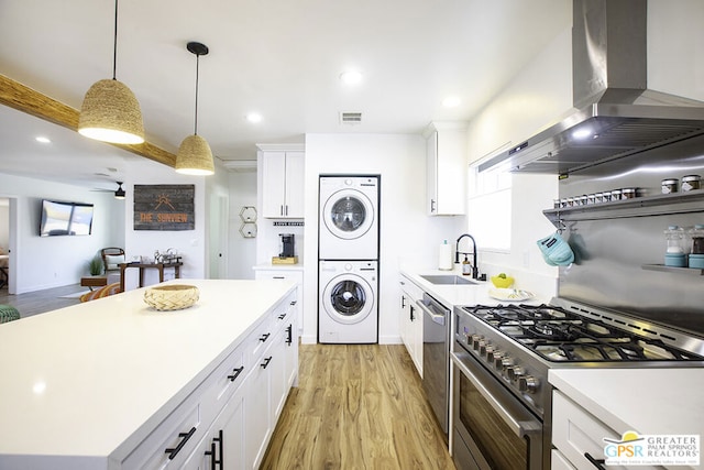 kitchen featuring white cabinetry, sink, wall chimney exhaust hood, stainless steel appliances, and stacked washer / dryer