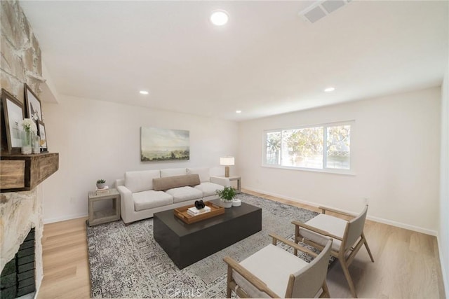 living room featuring light wood-type flooring and a stone fireplace