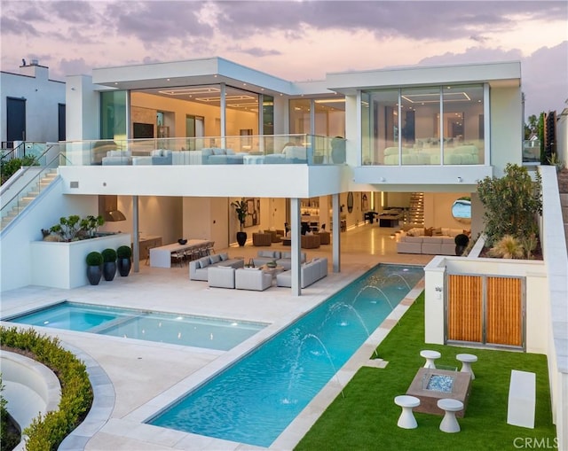 back house at dusk with an outdoor living space, a balcony, pool water feature, and a patio area