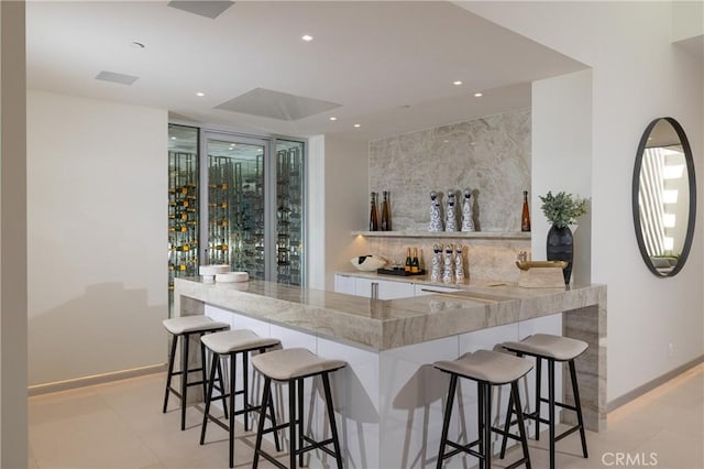 bar with white cabinetry, light stone counters, and light tile patterned floors