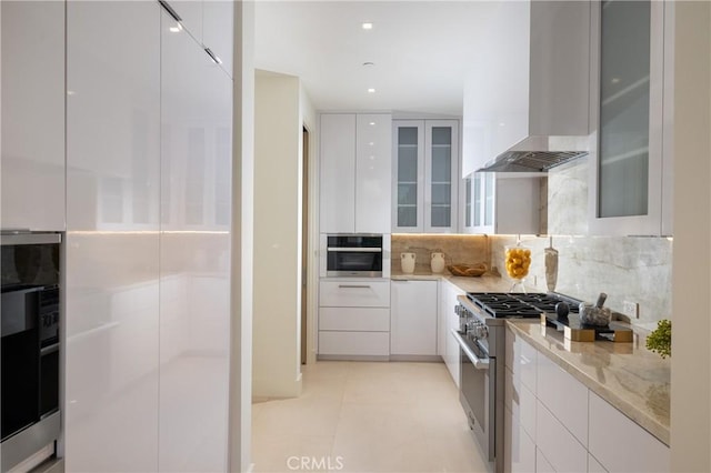 kitchen featuring white cabinets, decorative backsplash, stainless steel appliances, and wall chimney exhaust hood