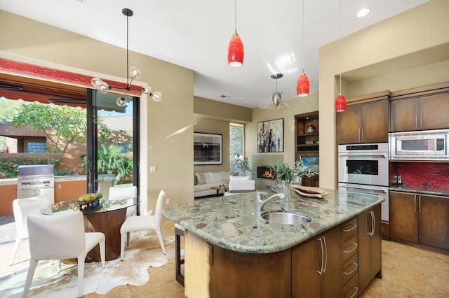 kitchen featuring stainless steel appliances, decorative light fixtures, light stone counters, and a kitchen island with sink