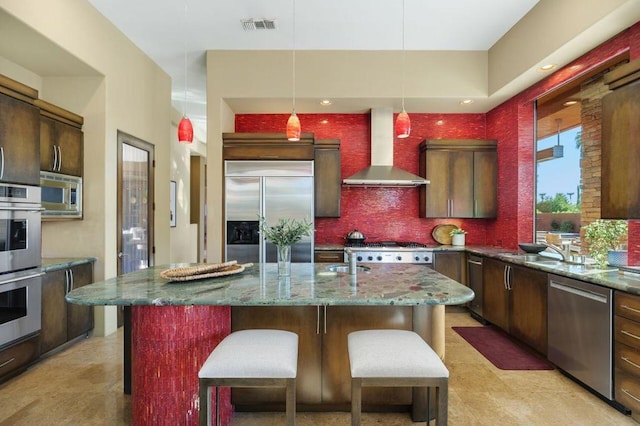 kitchen with built in appliances, wall chimney range hood, and a kitchen island with sink