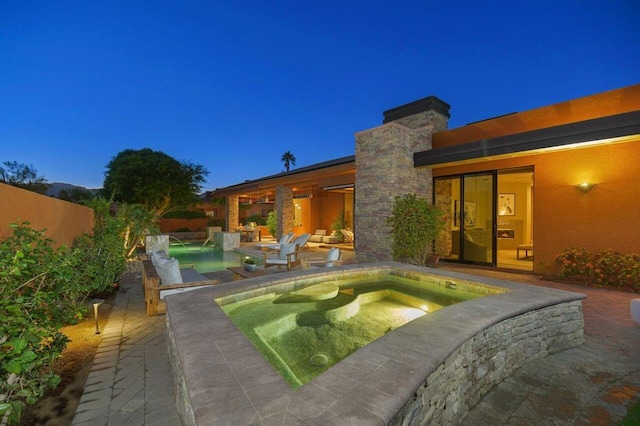 pool at dusk featuring pool water feature, a patio area, and an in ground hot tub