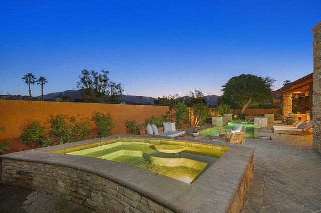 pool at dusk featuring a patio area, an in ground hot tub, and a mountain view