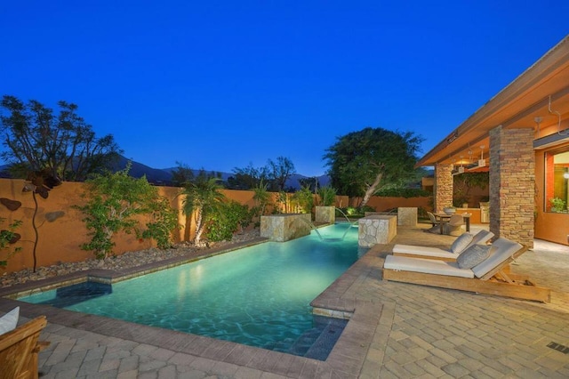 pool at dusk with pool water feature and a patio area