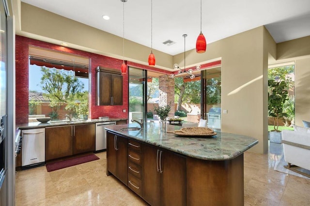 kitchen featuring dishwasher, light stone countertops, plenty of natural light, and an island with sink