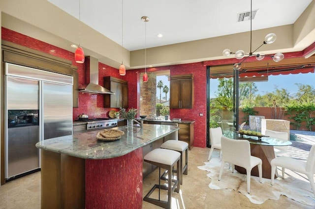 kitchen with a center island, wall chimney range hood, decorative backsplash, dark stone countertops, and stainless steel appliances