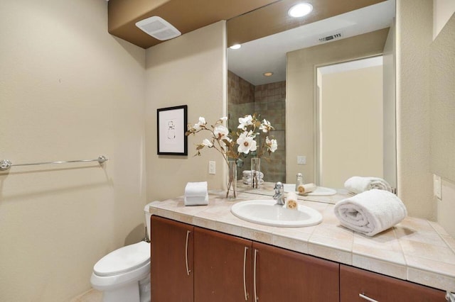 bathroom with a tile shower, vanity, and toilet