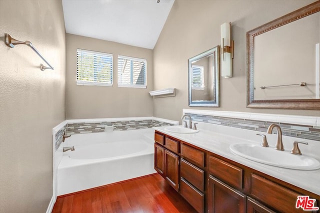 bathroom with a bathing tub, backsplash, hardwood / wood-style floors, lofted ceiling, and vanity