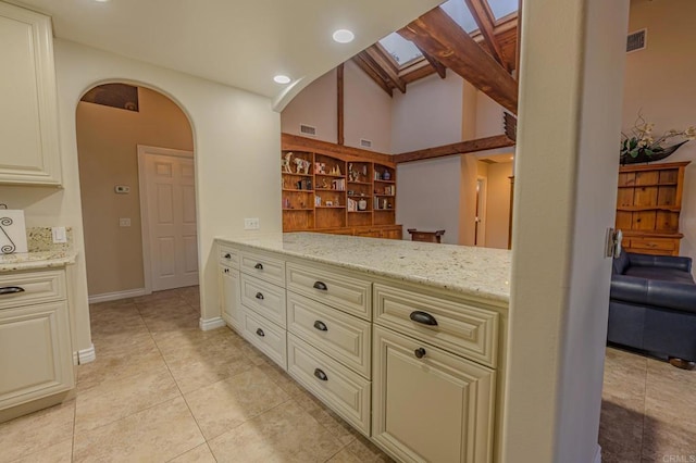 kitchen with light stone counters, light tile patterned floors, cream cabinets, and lofted ceiling with skylight