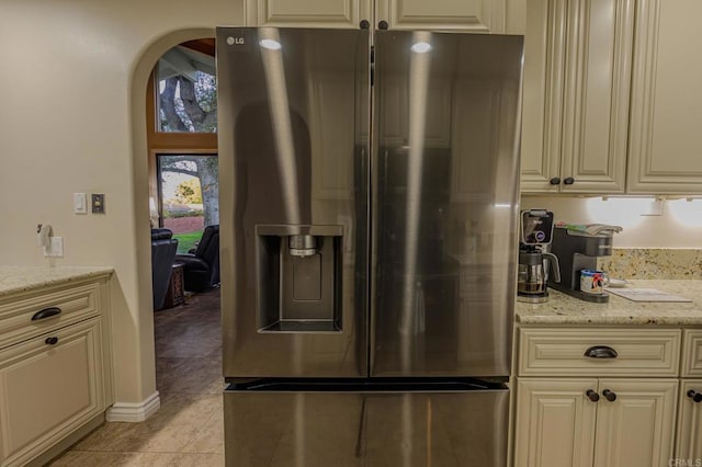 kitchen featuring stainless steel refrigerator with ice dispenser, cream cabinets, light stone countertops, and light tile patterned flooring