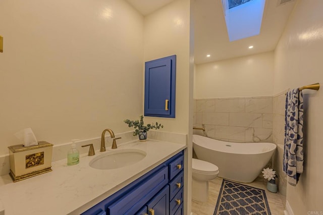 bathroom with toilet, a skylight, tile walls, vanity, and a washtub