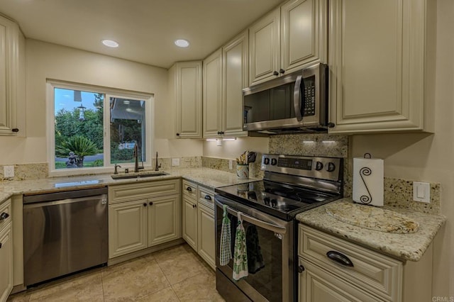 kitchen with appliances with stainless steel finishes, light tile patterned flooring, a sink, and light stone countertops